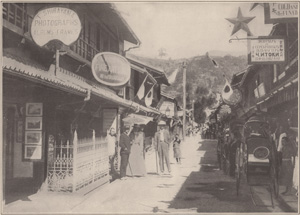 STREET SCENE IN NAGASAKI, WITH JINRIKISHAS ON THE RIGHT